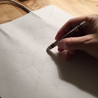 Drawing a white spider web onto a white craft bag with a white crayon