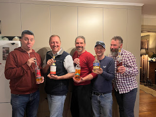 Five men holding whisky bottles in a kitchen.