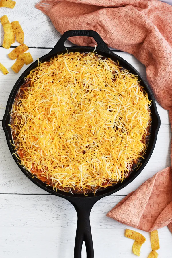 Shredded cheese covering the cooked beef mixture in a cast iron skillet, for a gooey and melted cheese topping