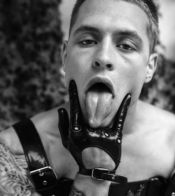 Black and white fashion photo from the head up of sexy model sticking tongue out through tight black leather driver gloves while making symbol for eating pussy.