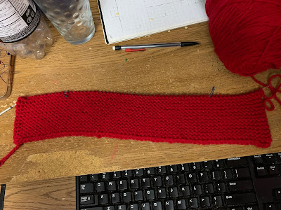 A piece of red garter stitch knitting on a circular knitting needle. The piece is much wider than it is tall.