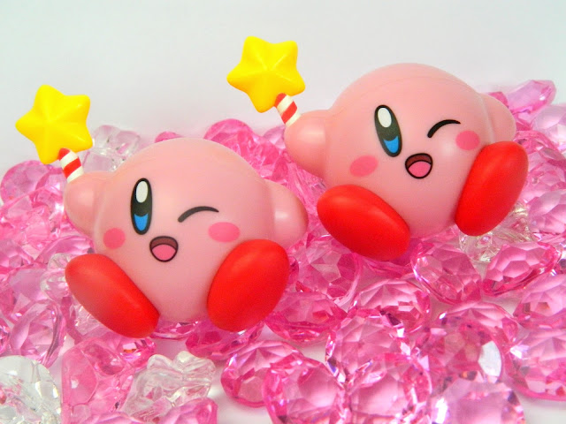 Two Nintendo Kirby figures holding star-wands and sitting on plastic gems 