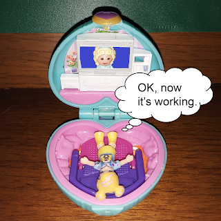 Polly Pocket doll lies on fold-out-sofa staring at television screen with a face showing on it, thinking, "OK, now it's working." 