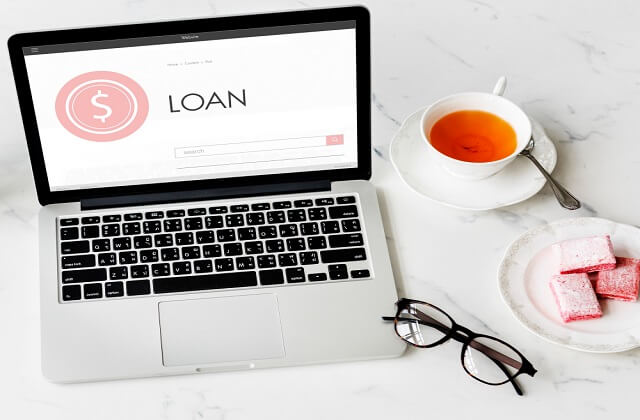 laptop with loan text on the screen eyeglasses and pink pastries on the desk