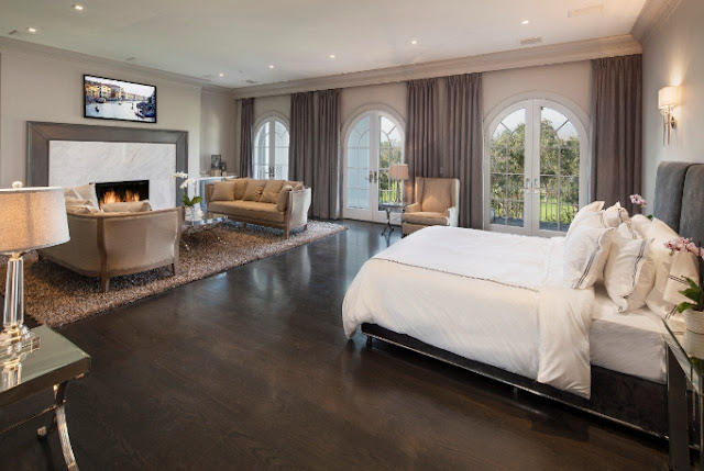 brown bedroom upholstered headboard bedding with navy piping wood floor shag rug fireplace dueling sofa arched French doors balcony