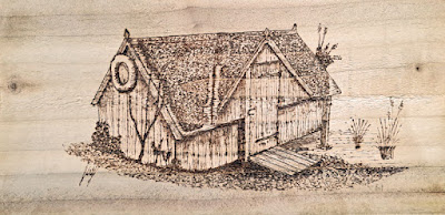 a photo of a drawing of an old boathouse drawn on wood using a wood burner