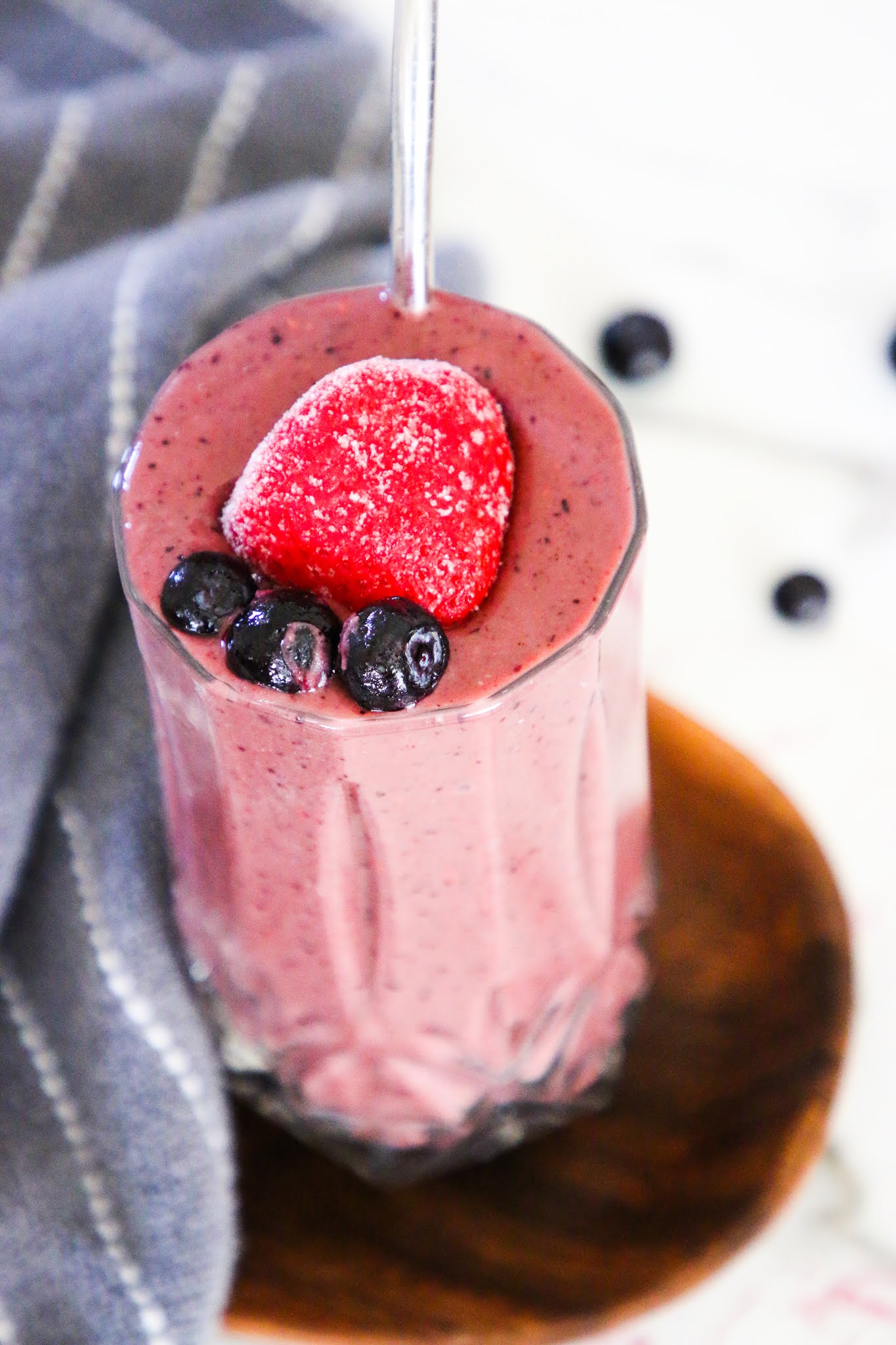 Smoothie with a big strawberry on top, sitting on a wooden platter, with a dish towel in the background.