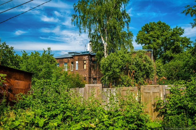 Огороды за забором из дверей на фоне кирпичного здания