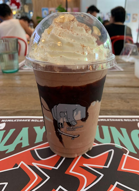 Chocolate banana milkshake with whipped cream in a plastic dome cup