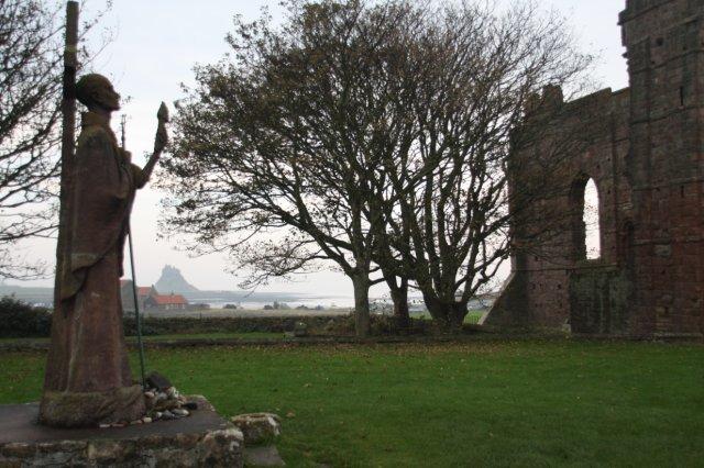 La Isla Sagrada de Lindisfarne The Holy Island of Lindisfarne – Monasterio de Lindisfarne y Estatua de San Aidan. Al fondo, Castillo de Lindisfarne