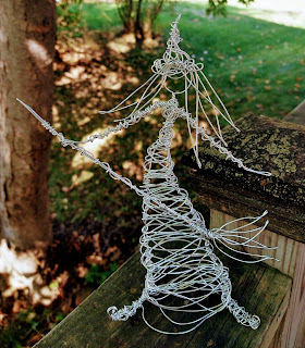 A loosely wrapped figurative sculpture of a silver-wire witch holding a broom by Joni B.