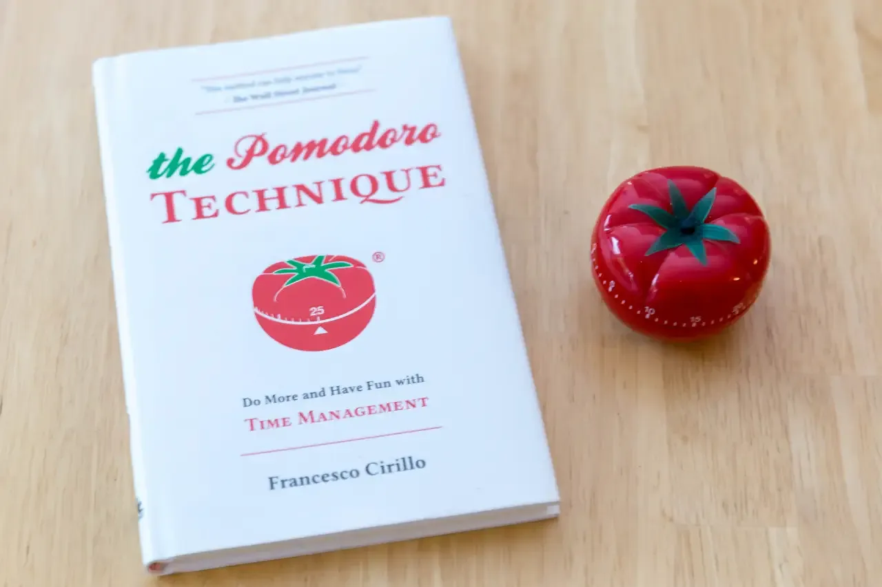 Livro 'The Pomodoro Technique' ao lado de um timer de cozinha pomodoro.