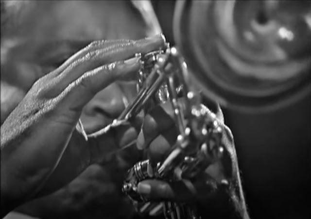 Screenshot up very close to Harry "Sweets" Edison's hands while he plays his trumpet in a black and white filmed concert in England in 1964.
