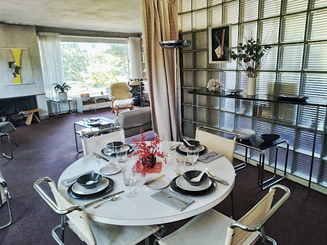 A view that captures almost the entire dining room in the foreground (including the dining table view) and living room in the background (including the fireplace view to the left, and the radio console plus long chair on the right).