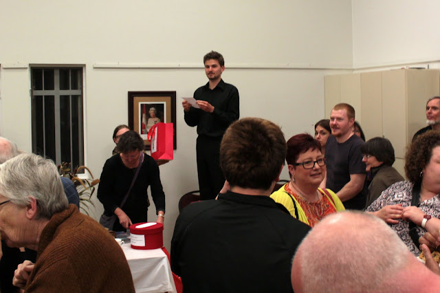 Alasdair stands on a chair to see over the crowd and announce the door prize winner