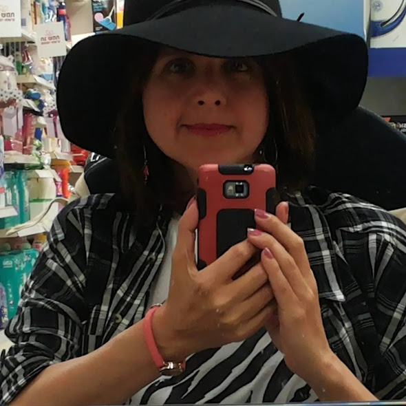 אני לובשת חולצה עם משבצות שחור-לבן, חובשת כובע שחור רחב שוליים, מחזיקה טלפון ומצלמת את דמותי הנשקפת מהמראה.