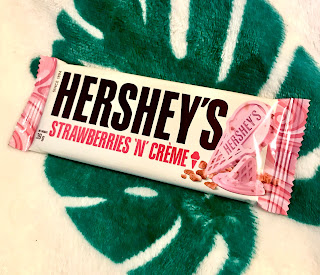 A rectangular pale pink rectangular chocolate bar with little white sugar crystals running throughout in a white rectangular packet with Hersheys in bold black font with strawberries and creme underneath in pink small font on a bright background 