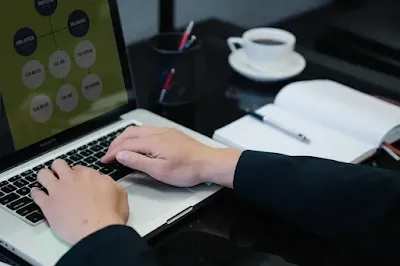 شخص يكتب على لابتوب في بيئة عمل حديثة، مع فنجان قهوة بجانبه، بينما تظهر على الشاشة رسومات تشير لاستخدام الذكاء الاصطناعي في كتابة المحتوى.