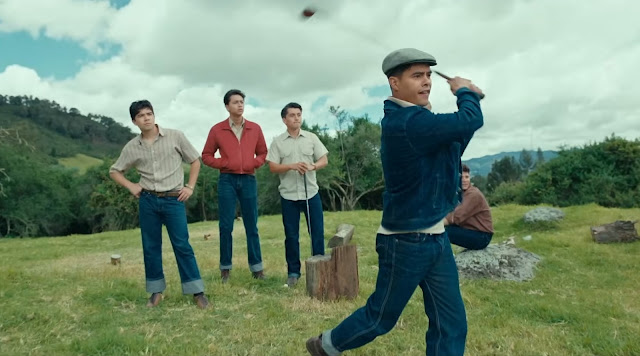 A man swings a golf club while three other men watch