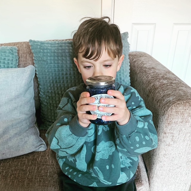 Little boy holding a jam jar filled with water, glue and blue glitter