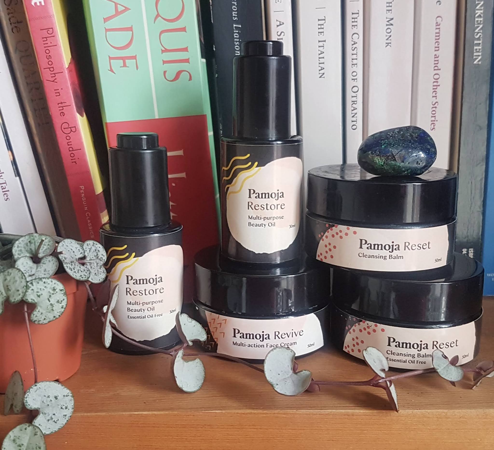 Pamoja Skincare collection on a bookshelf surrounded by vining plants