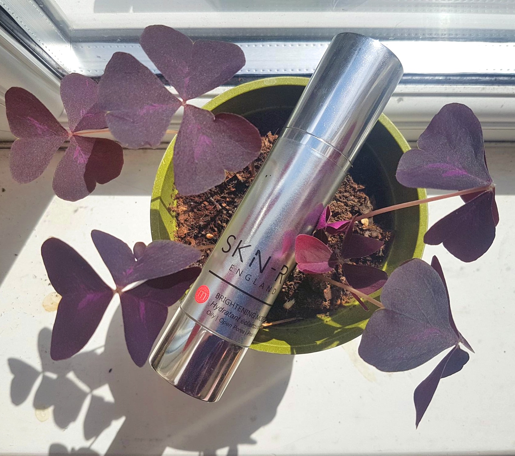 Skn-RG Advanced Brightening Moisturiser on top of a purple oxalis plant