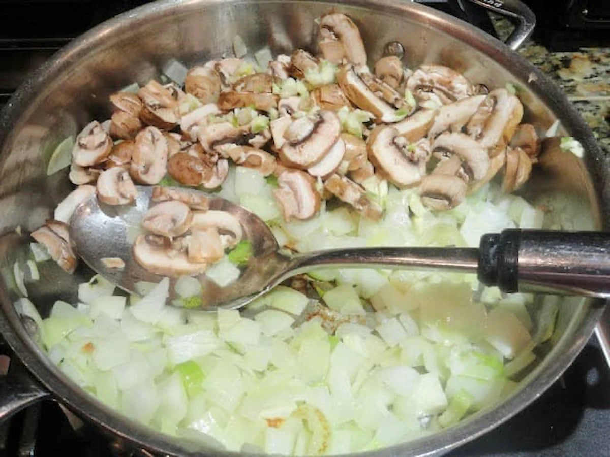 Sautéed onion, celery, and mushrooms in a stainless steel pan.