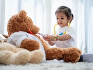 Little girl wearing a stethoscope pretend playing to be a doctor is treating her big brown teddy bear patient.