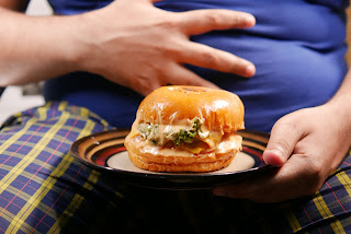 a person holding their stomach and holding a plate with a burger on it