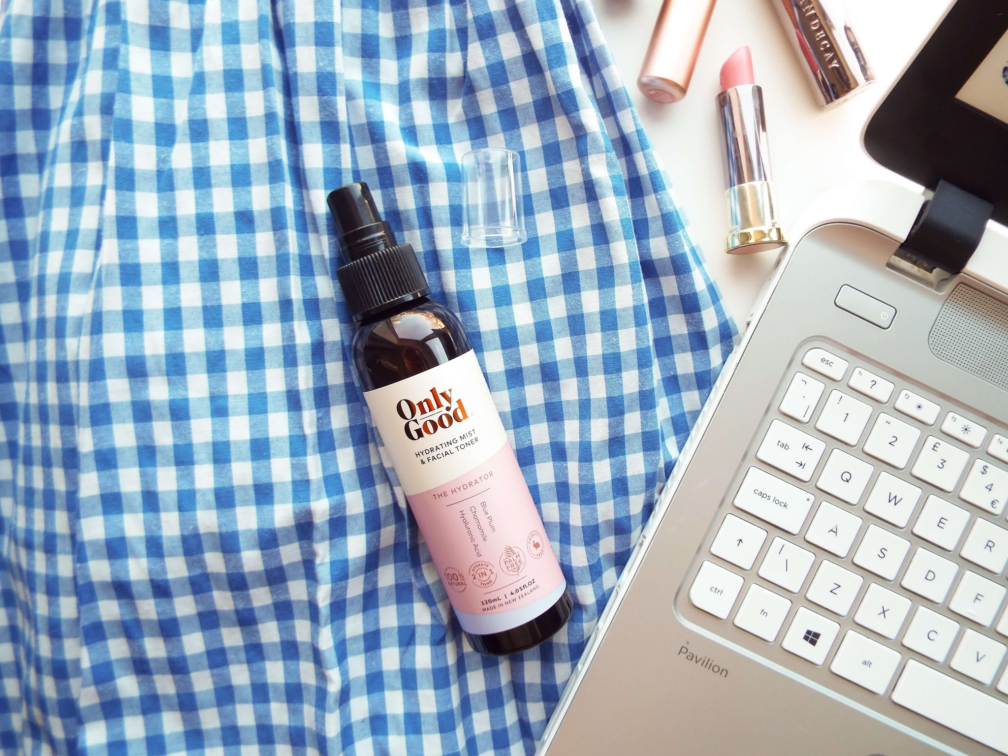 Close up of flatlay, focusing on skincare sat on dress, with laptop keyboard to the left.