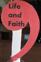 red comma on a stick, words Life & Faith printed on comma