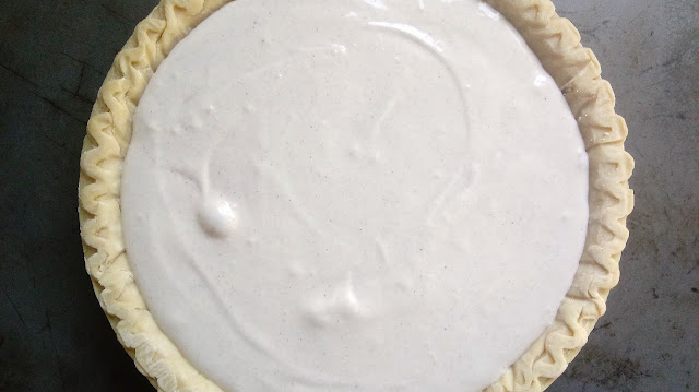 A spiced sour cream mixture sitting on top of apple pie filling in a frozen pie crust