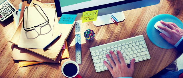 birds eye view of desk with desktop, coffee, folders, glasses, and calculator