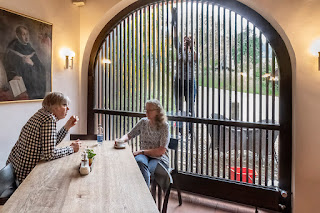 Hotelgäste im Gespräch, während eine Angestellte die Fenster putzt.