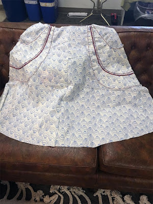 The front panel of a skirt with big swoosh-shaped patch pockets, in white fabric with blue seashell outlines. Half the skirt has the pattern right side up, and the other half has it upside down, with the pockets opposite their respective sides. The red topstitching on the pockets shows up especially well.