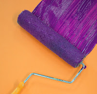 A purple roller beginning to paint an orange wall.