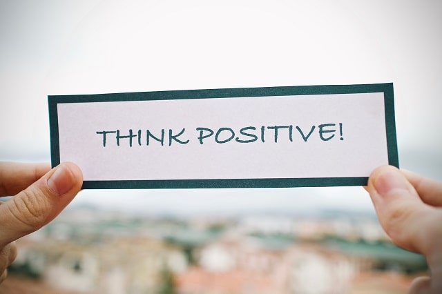 THINK POSITIVE!と書かれた紙を両手で持つ人