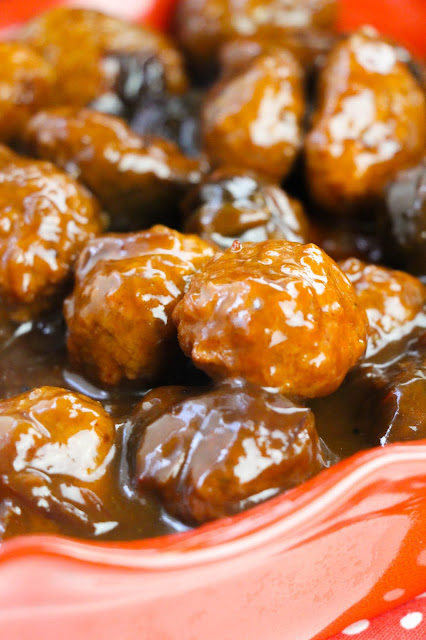 meatballs scooped by a spoon in a red casserole dish.