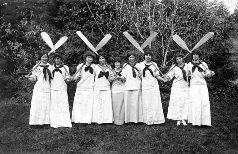 Women with canoe paddles dressed for the chorus of the musical 
