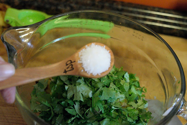 A measuring spoon with salt in it, over the bowl of cilantro. 