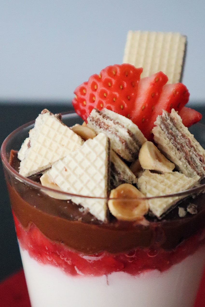 glass of mascapone mousse with strawberries, chocolate hazelnut cream, pieces of wafers, hazelnuts and a strawberry