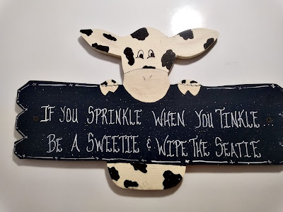 A cow holding a plaque that reads… IF YOU SPRINKLE WHEN YOU TINKLE, BE A SWEETIE & WIPE THE SEATIE