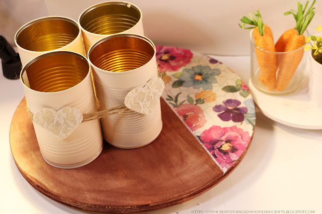 Four metal cans with twine and fabric hearts on top of round wooden board displayed on a table