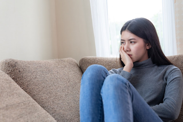 Close up face of unhappy asian pretty young woman sitting alone on couch