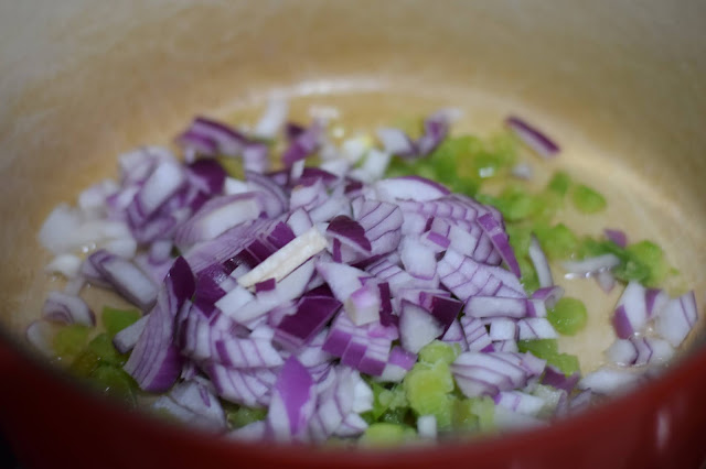 The bell pepper and purple onion sautéing in a pot.