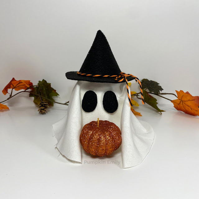 A DIY ghost holding a pumpkin and wearing a witch hat.