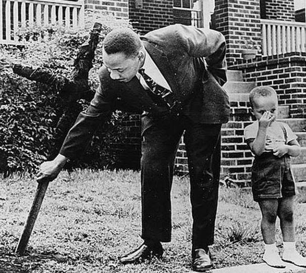 Мартин Лютер Кинг с его сыном убирающие обгоревший крест во дворе их дома, 1960 г.