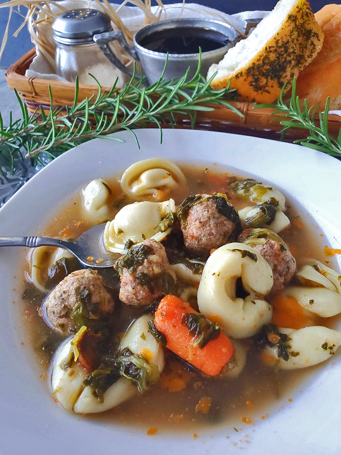 This is a white bowl full of Italian meatballs, spinach in a hearty chicken broth