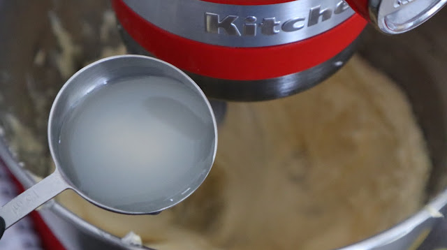 Adding in the lemon juice into the buttercream located in a silver kitchen aid bowl