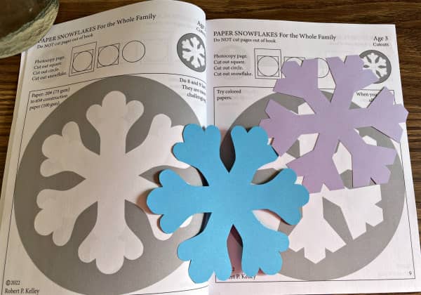 open snowflake template book with two colorful paper snowflake examples placed on top